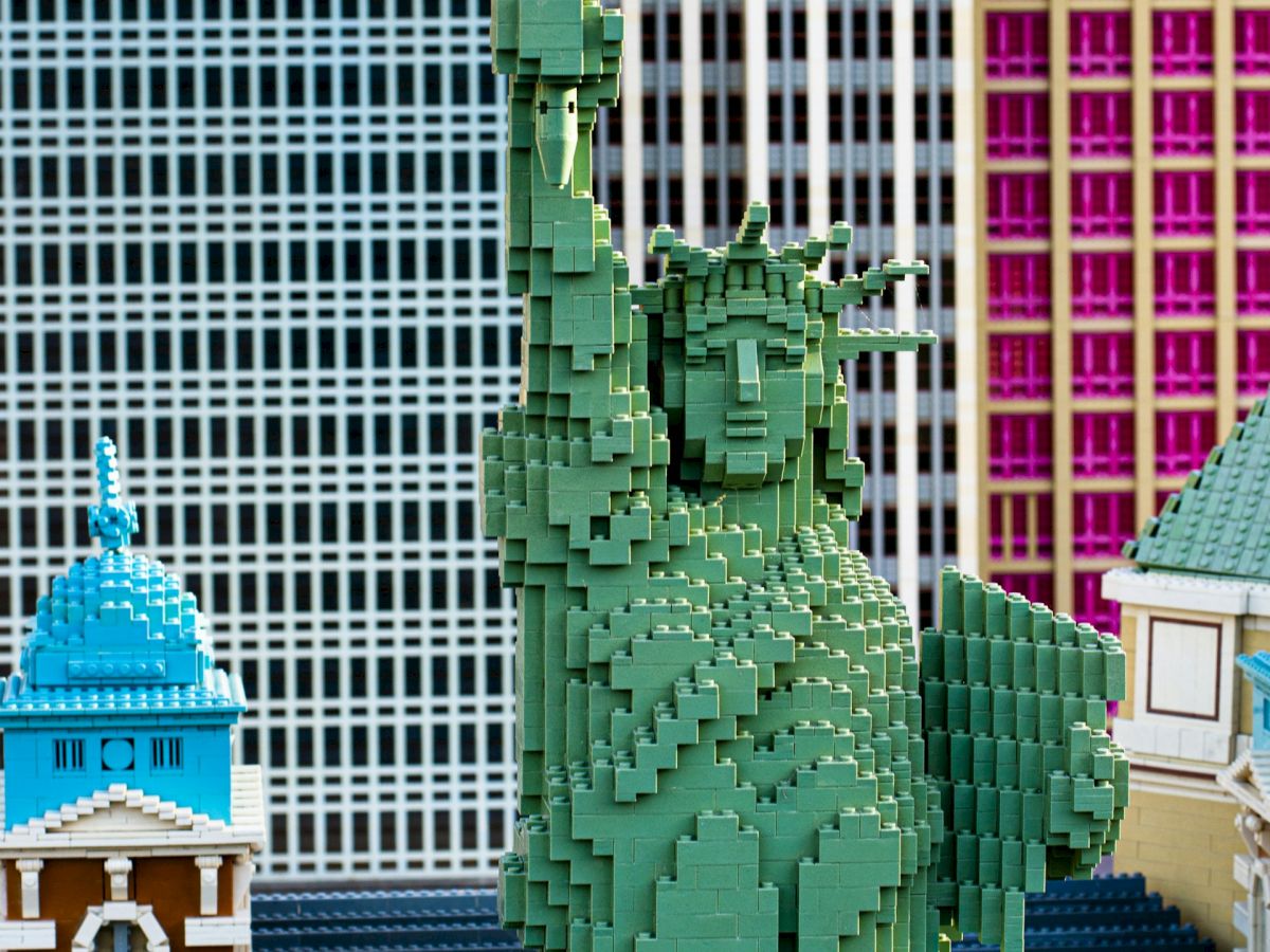 The image shows a Lego model of the Statue of Liberty with colorful buildings in the background.