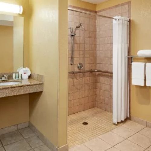 This image shows a clean, well-lit bathroom with a sink, a walk-in shower with a curtain, and a toilet with towels hanging on a rack.